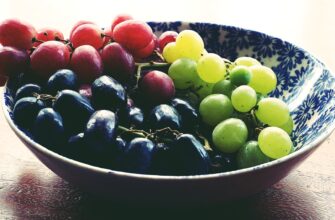 red black and green grapes in round blue and white floral ceramic bowl