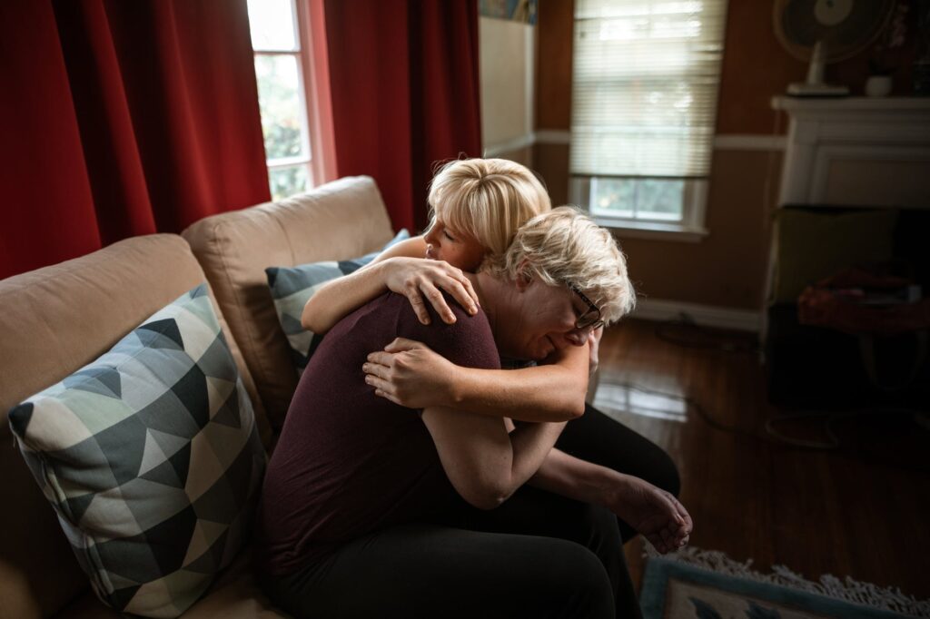 woman embracing crying elderly woman while sitting on couch