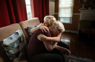 woman embracing crying elderly woman while sitting on couch