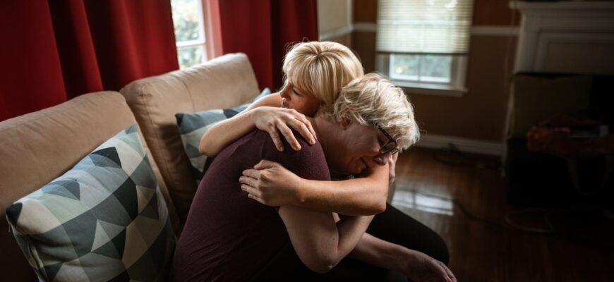 woman embracing crying elderly woman while sitting on couch