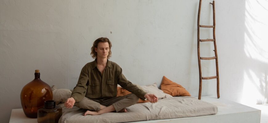 peaceful man meditating on bed in lotus pose