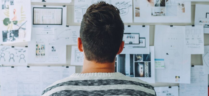 man wearing black and white stripe shirt looking at white printer papers on the wall