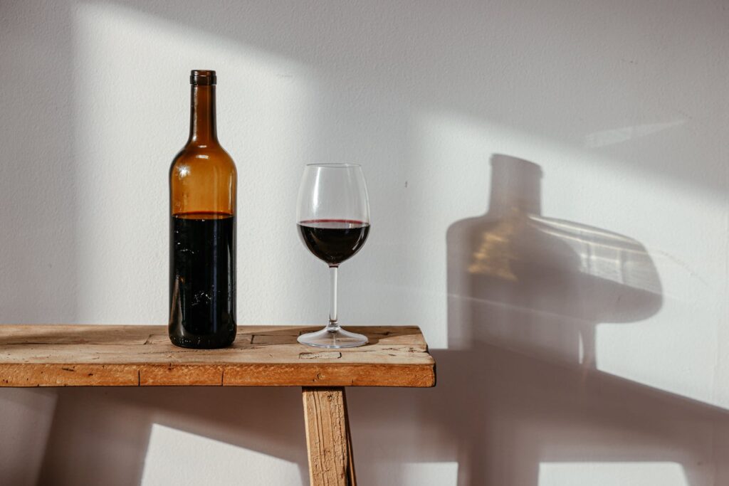 a bottle and a glass of wine on a wooden bench