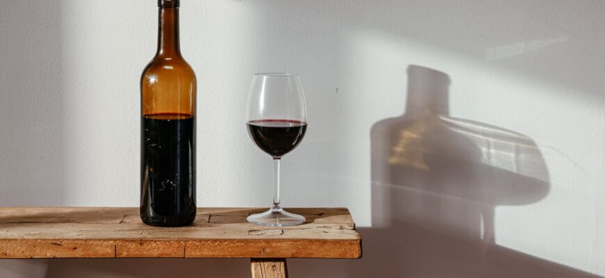 a bottle and a glass of wine on a wooden bench