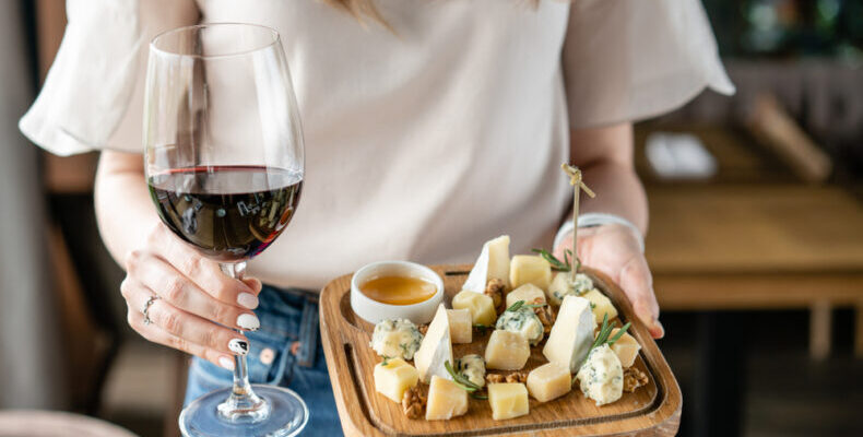 o femeie care tine in mana un platou cu branzeturi si un pahar cu vin 790x460 1