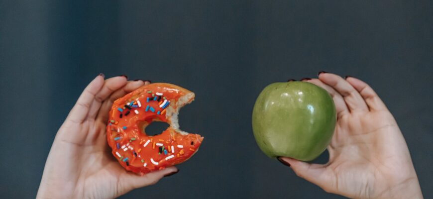 faceless woman showing fresh apple and sweet doughnut