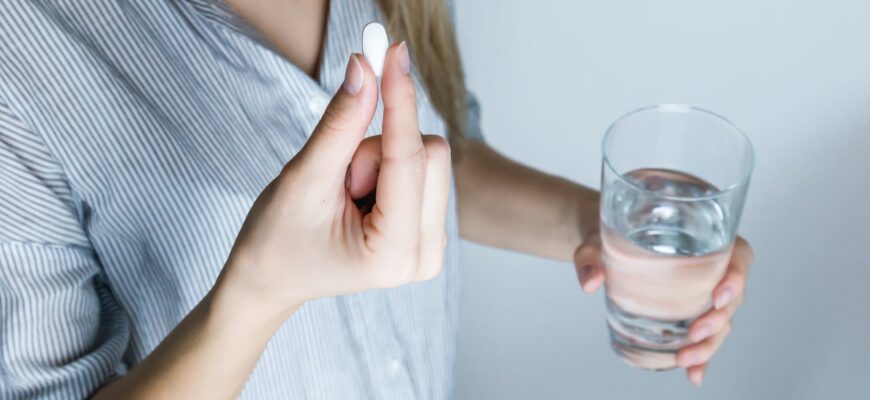 woman holding half full glass and white medicine pill