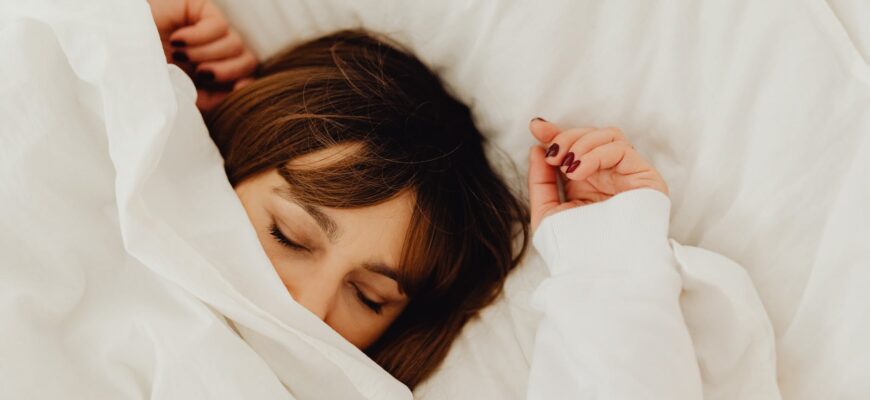woman lying on bed covering her face with a white blanket