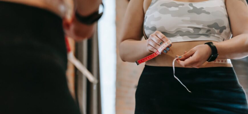 woman measuring waist with tape in gym