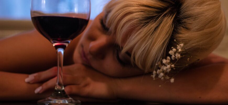 woman with white flower accent headdress leaning her head on table beside half filled wine glass