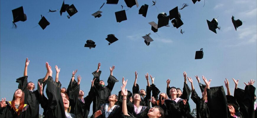 newly graduated people wearing black academy gowns throwing hats up in the air