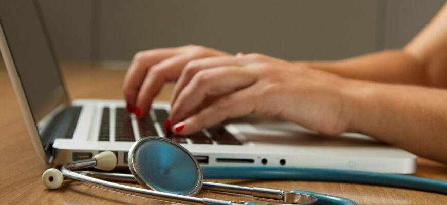 person sitting while using laptop computer and green stethoscope near