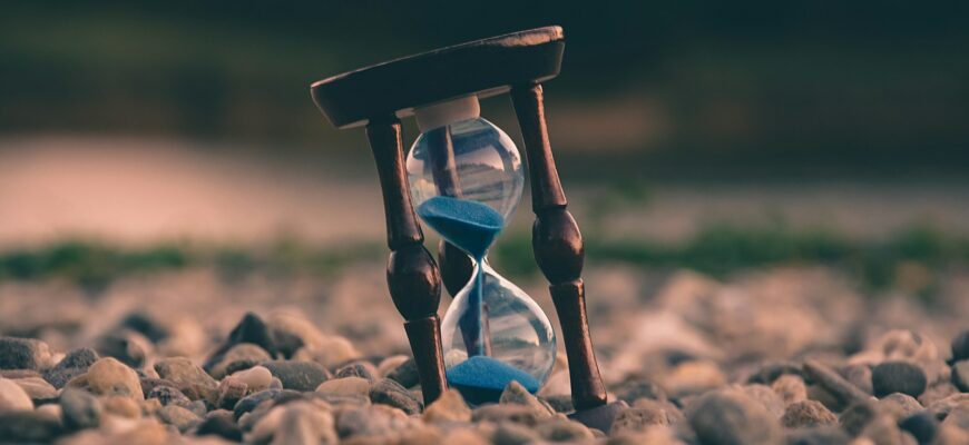 selective focus photo of brown and blue hourglass on stones