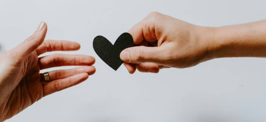 person reaching black heart cutout paper